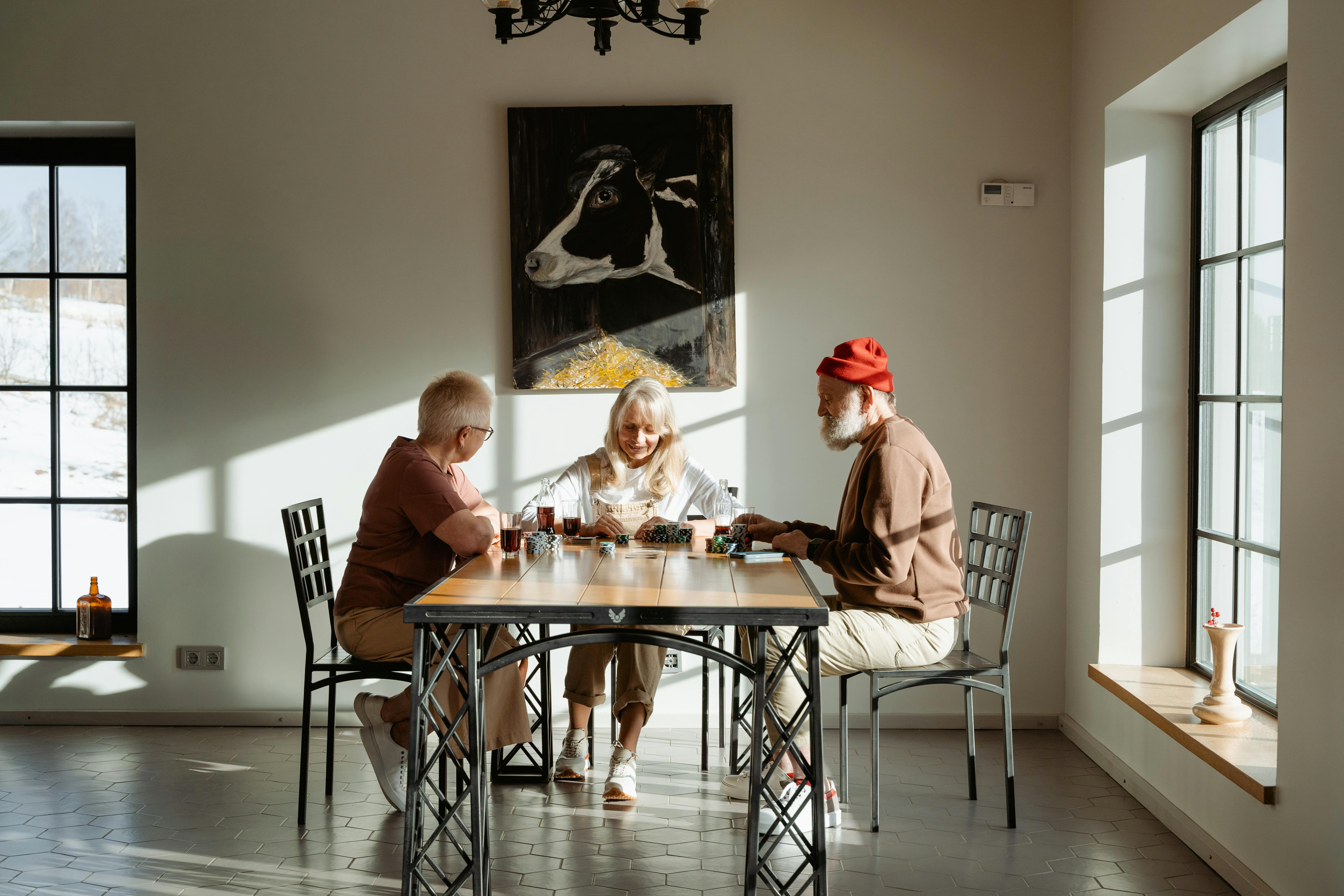 Three senior adults playing a board game indoors, enjoying togetherness and sunlight.